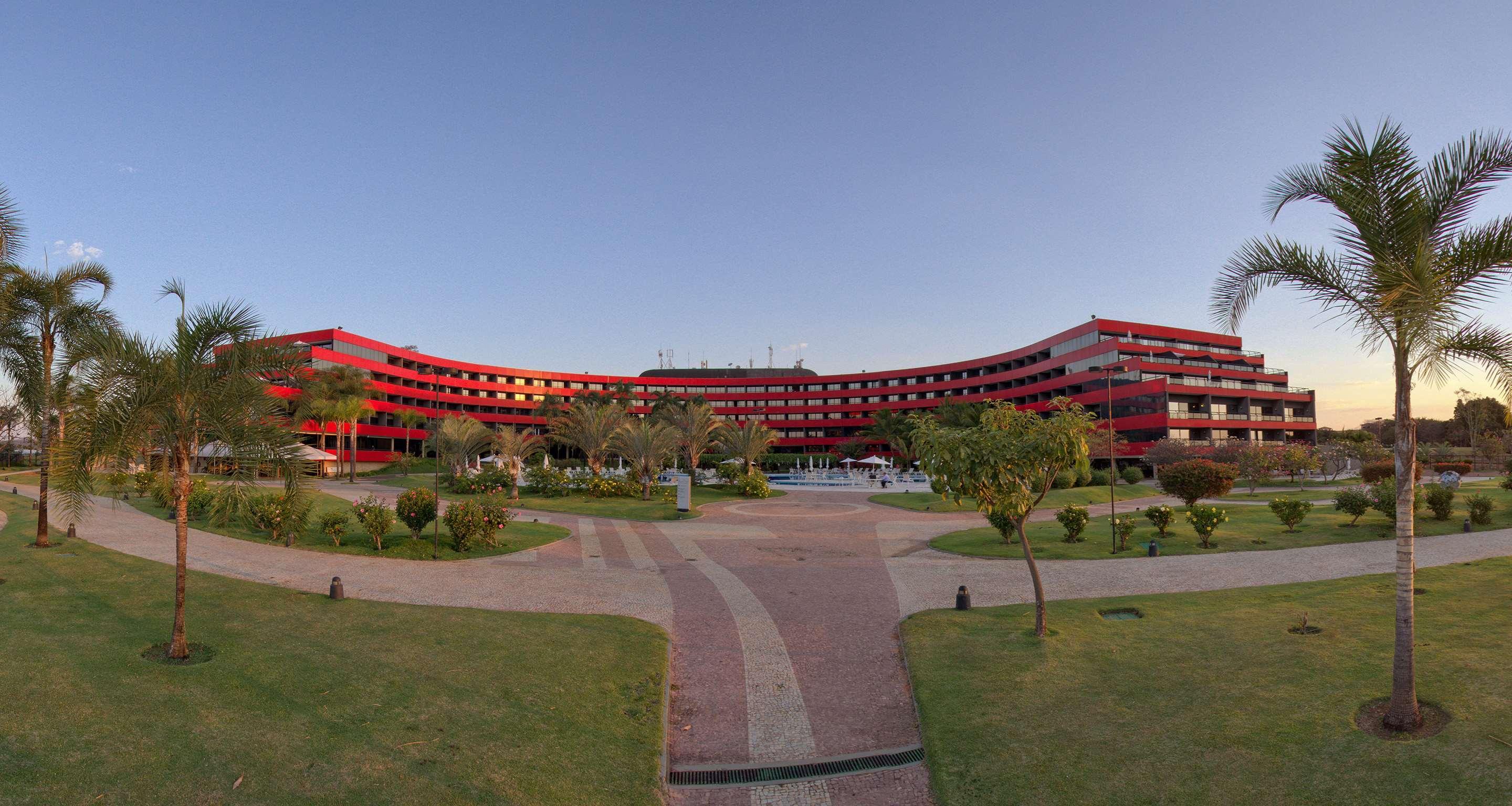 Royal Tulip Brasilia Alvorada Hotel Ngoại thất bức ảnh The photo shows a large, curved building with a vibrant red exterior. It appears to be a hotel or resort, surrounded by well-maintained gardens and green spaces. The landscape includes manicured lawns, small trees, and pathways, suggesting a pleasant